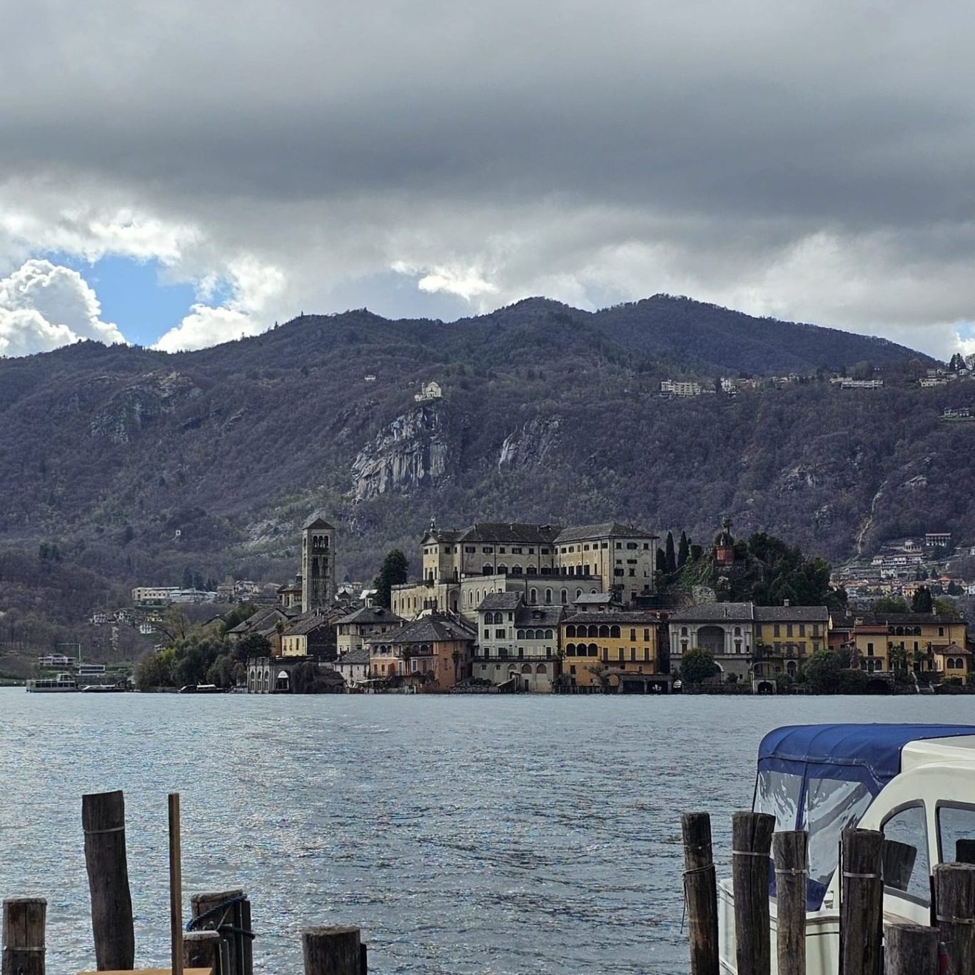 Blick auf eine Stadt am See mit einem Schloss und Bergen im Hintergrund unter bewölktem Himmel.