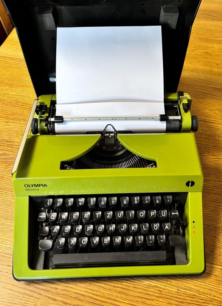 Grüne Schreibmaschine mit Papierblatt und schwarzer Tastatur auf holzigem Tisch.